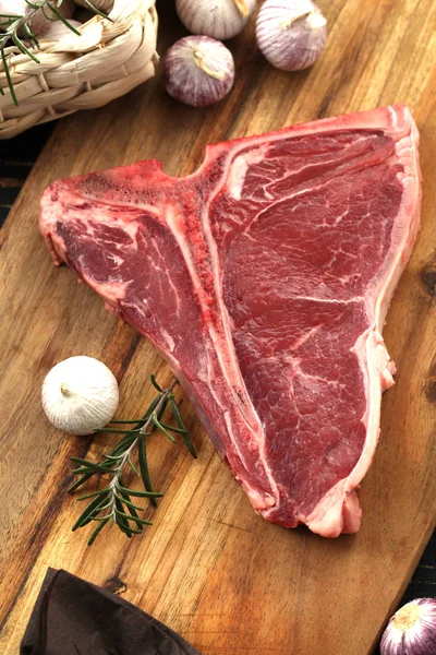 Nyers T-bone steak fűszerekkel fűszerezett, friss fűszernövények tálalva — Stock Fotó