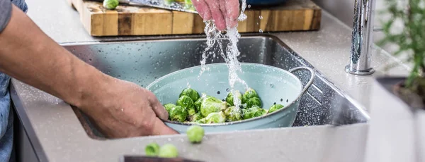 partial view of person washing raw Brussels sprouts in kitchen sink