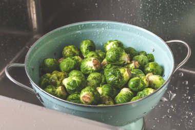 close-up view of fresh green Brussels sprouts in colander washing in sink clipart