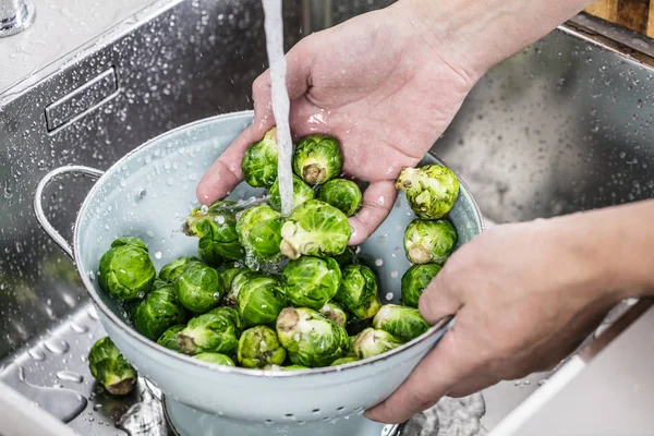 cropped shot of person washing raw Brussels sprouts in kitchen sink