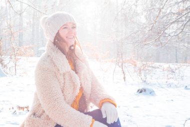 güzel oturan genç kadın gülümseyerek ve uzak kış ormanda arıyorsunuz