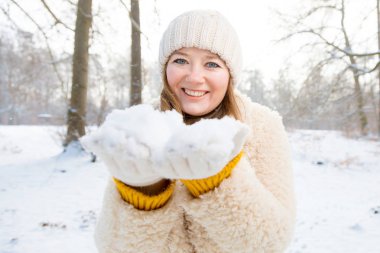 Güzel genç bir kadın kış ormanında kameraya gülümsüyor. 