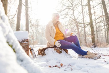 Güzel, gülümseyen genç bir kadın kış ormanında oturuyor.