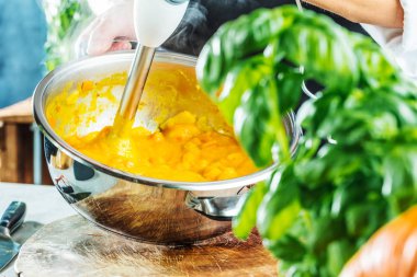 Balkabağı çorbasını karıştırıcıyla hazırlayan kişinin kısmi görüntüsü