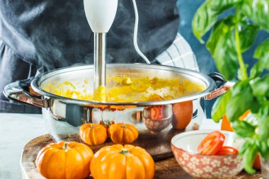 Balkabağı çorbasını karıştırıcıyla hazırlayan kişinin kısmi görüntüsü