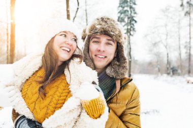 Mutlu genç çift, kış ormanında birbirlerine sarılıyorlar.