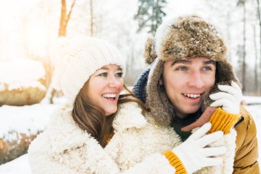 Mutlu genç çift, kış ormanında birbirlerine sarılıyorlar.