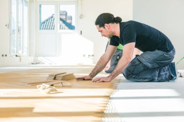 Ev tadilatı sırasında meşe parke döşemesi kuran konsantre adam  