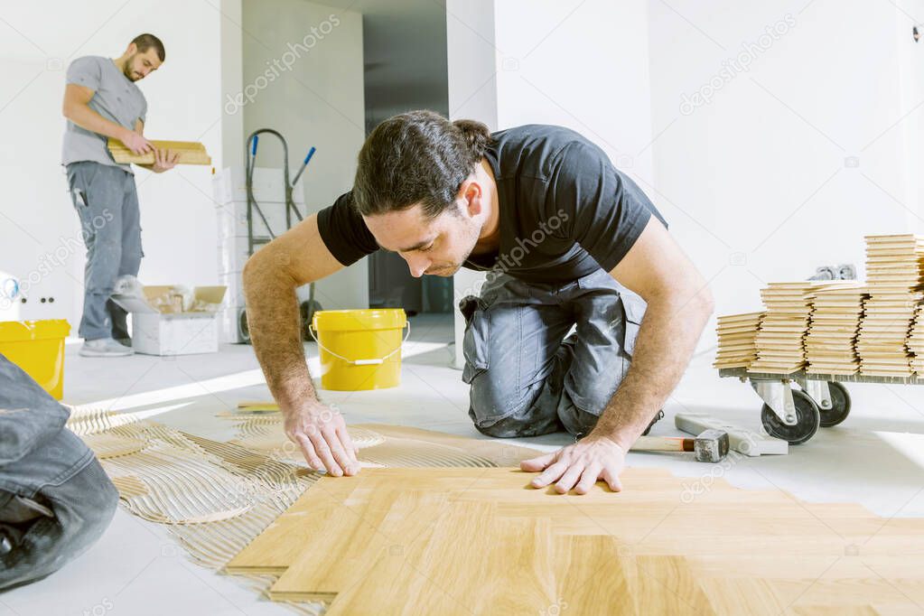 professional workers installing oak parquet floor during home improvement  