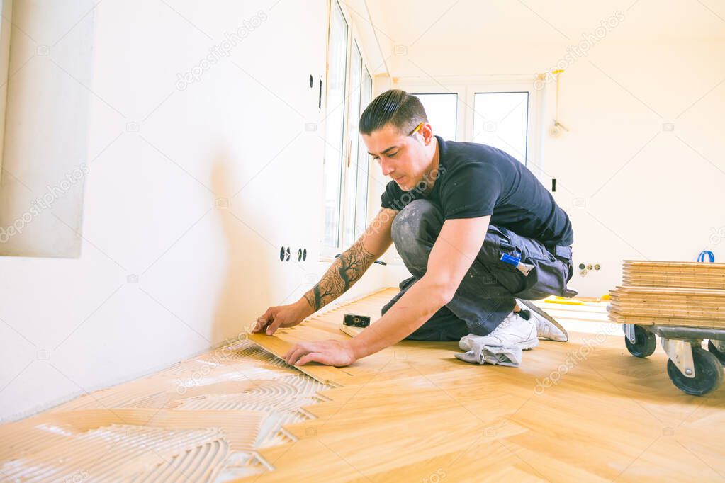 man installing oak parquet wooden floor during home improvement  