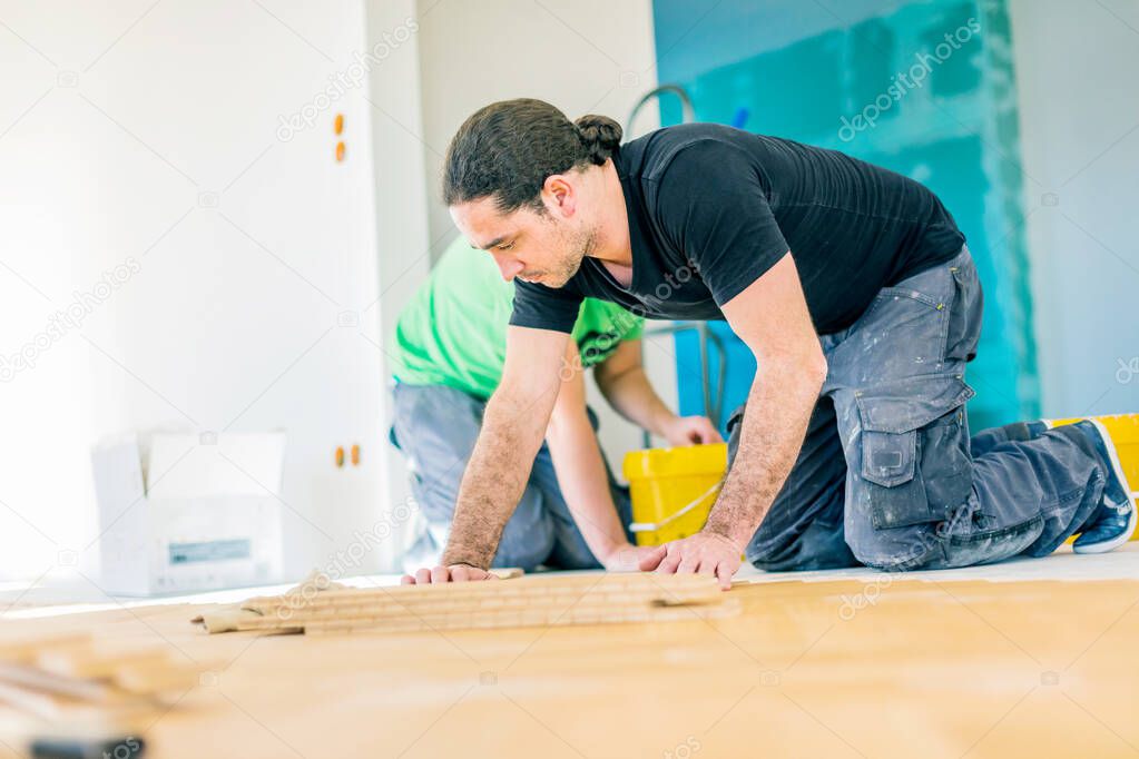 focused workers installing oak parquet floor during home improvement  