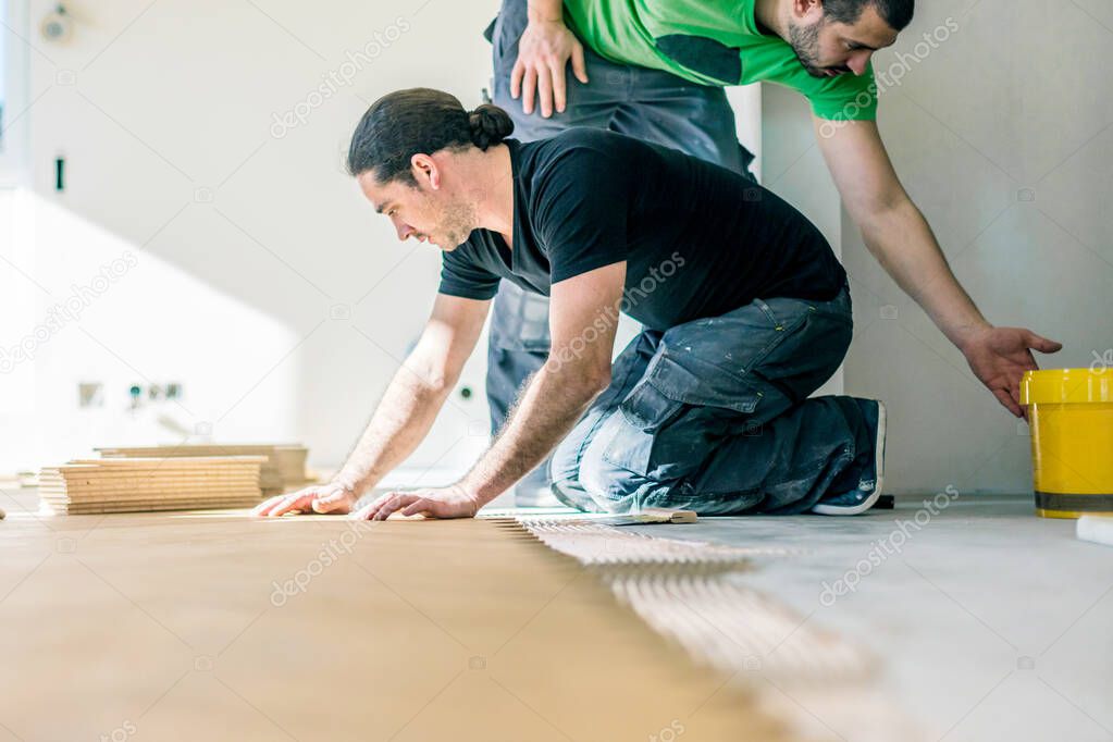 men installing oak parquet floor during home improvement  