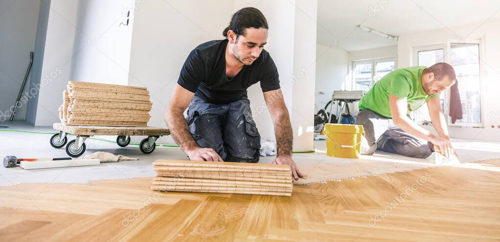 handymen installing oak parquet floor during home improvement  