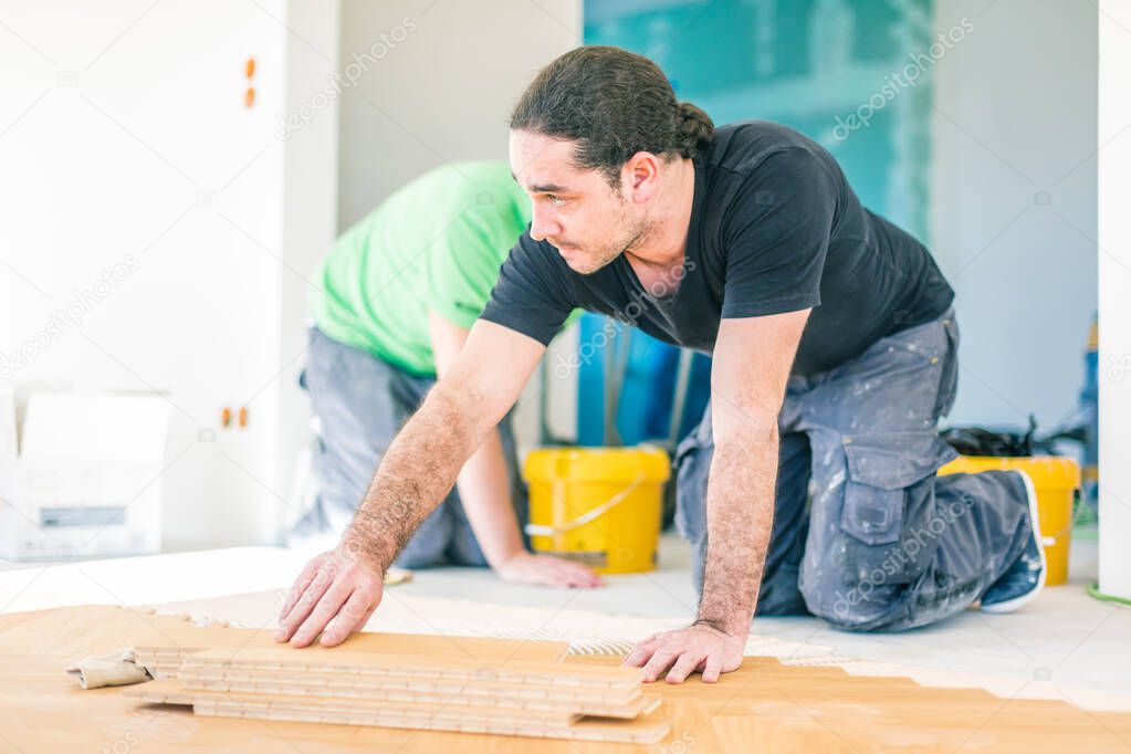young male workers installing oak parquet floor during home improvement  