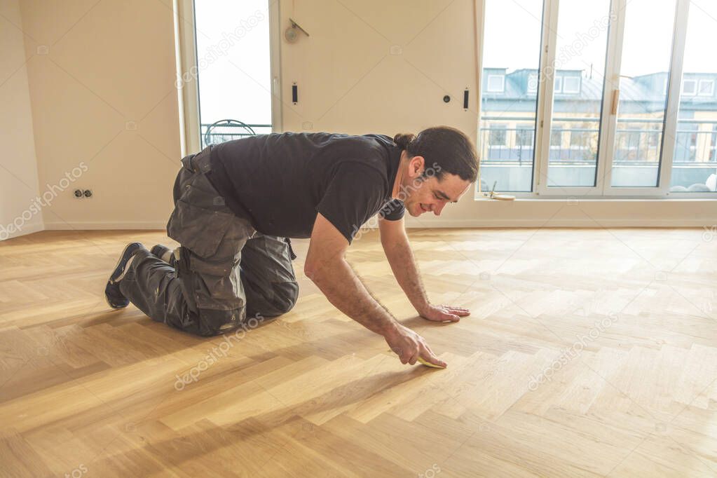 smiling man varnishing oak parquet floor during home improvement