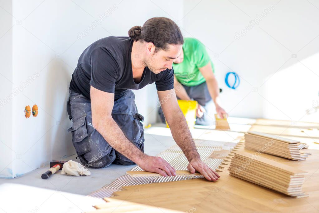 young male workers installing oak parquet floor during home improvement  