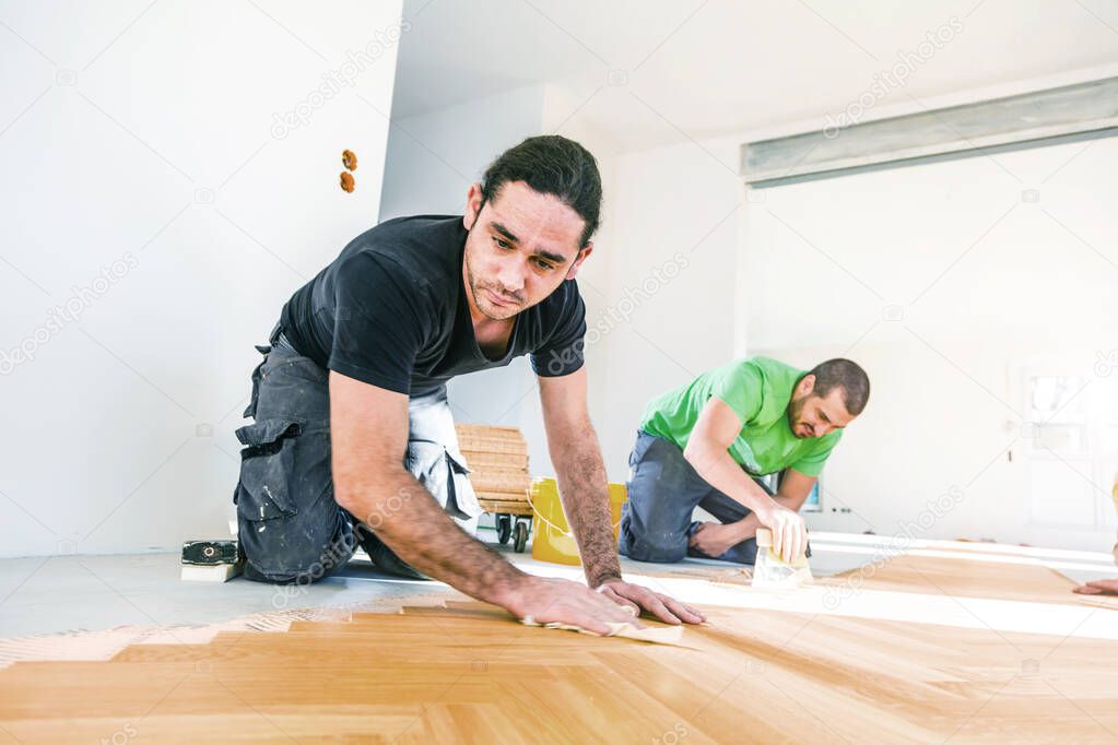 young workers installing oak parquet floor during home improvement  