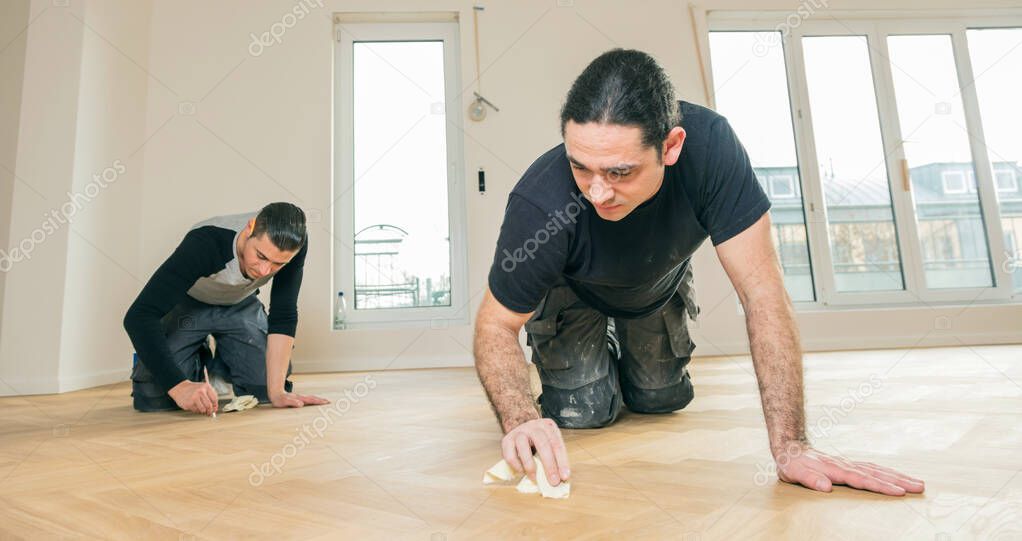 male workers varnishing oak parquet floor during home improvement