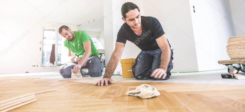 male workers varnishing oak parquet floor during home improvement