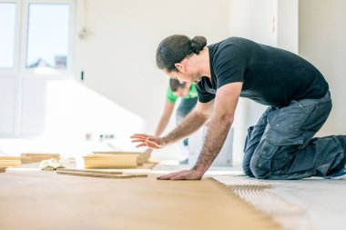 Ev tadilatı sırasında meşe parkesi döşeyen genç işçiler  