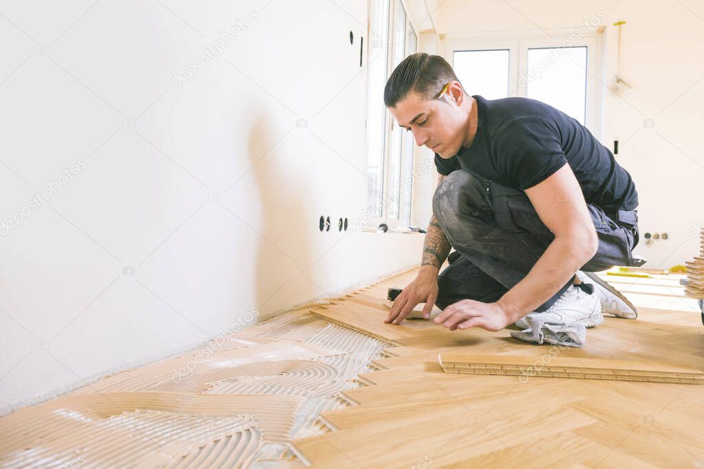 man installing oak parquet floor during home improvement   