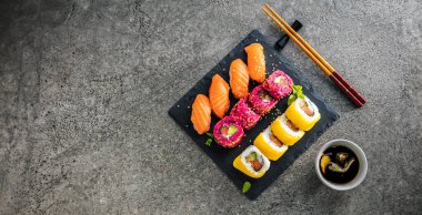 Gri yüzeyinde soya sosu ve çubuklu lezzetli suşi seti.