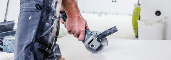 cropped shot of man cutting ceramic tiles with handy machine at the construction site indoors