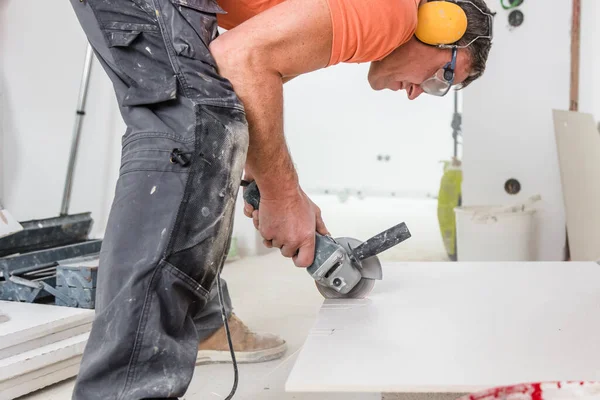 man cutting ceramic tiles with handy machine at the construction site indoors