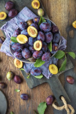Ahşap masa üzerinde yeşil yapraklı organik mor erikler