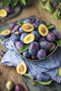 Ahşap masa üzerinde yeşil yapraklı organik mor erikler
