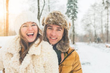 Mutlu genç çift, kış ormanlarında kameralara sarılıp gülümsüyor.