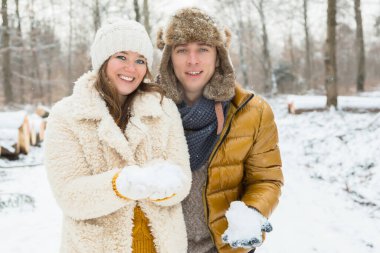Kartopu tutan ve kış ormanlarında kameraya gülümseyen neşeli genç çift.