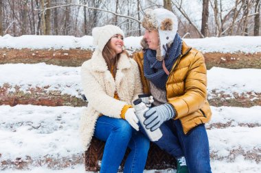 Mutlu genç çift birlikte oturuyor ve kış ormanlarında termostan sıcak içecek içiyorlar. 