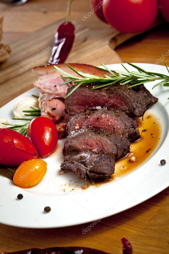 close-up view of delicious sliced grilled venison fillet with spices, herbs and vegetables on wooden table