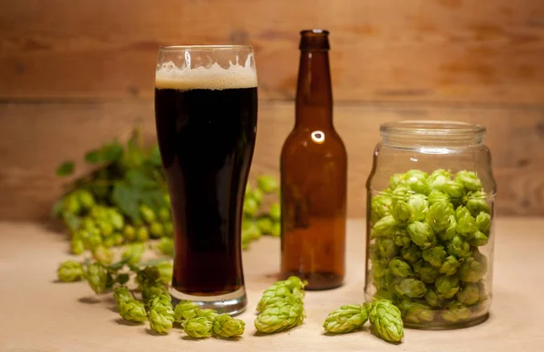 Glass of dark beer with green hop and bottle