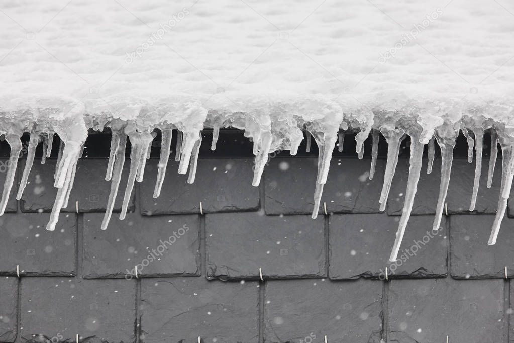 Ice stalactites with snow on a roof detail. Winter time. Horizontal