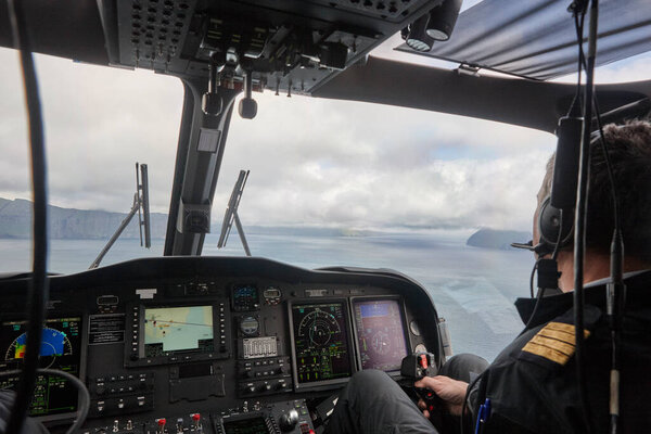 Helicopter cabin with pilots flying over Faroe Islands coastline. Denmark