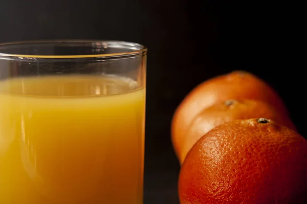 Glass of juice with three mandarin oranges over black background. Shallow dof.