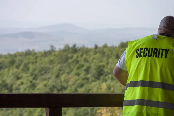 Security guard in yellow vest standing next to the railing with beautiful forest landscape view in the background. Copyspace.