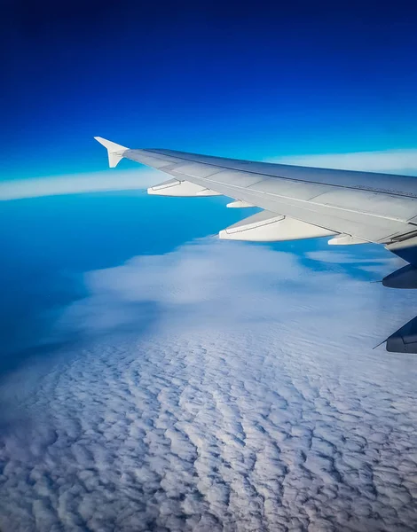 Photograph of the wing of an airplane from inside. Spectacular blue sky and lovely cloud formation.