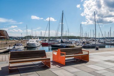 OSLO, NORWAY - 28 JULY, 2018: empty wooden benches on embankment and moored boats in harbour at Aker Brygge district, Oslo   clipart