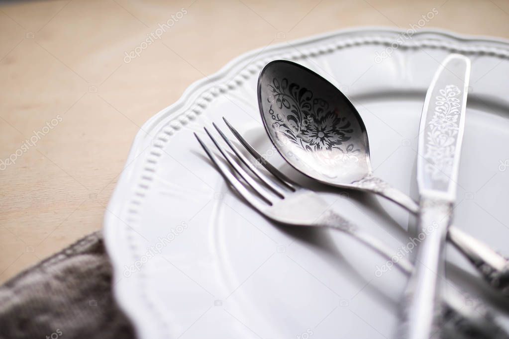 Cutlery on the white plate. Silver fork knife and spoon. Wooden table.