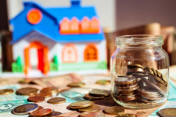 Szklany słoik z monetami na polu pieniądze i model domu na niewyraźne tło. Oszczędność pieniędzy na zakup koncepcji domu. — Zdjęcie stockowe