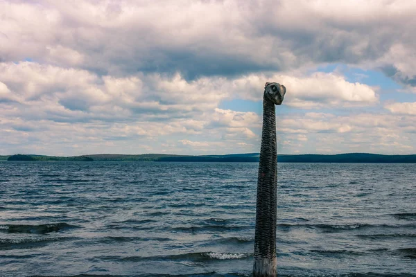 An old woodern sea monster totem in the lake under the cloudy sky. Siberian landscape.