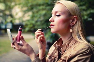 Güzel sarışın kadın sokakta dudaklarını tints.