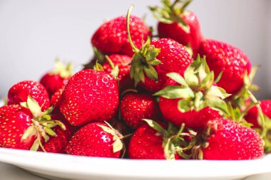 Beyaz bir tabak ve beyaz arka plan üzerinde olgun taze kırmızı çilek. Çilek yeni ürün.