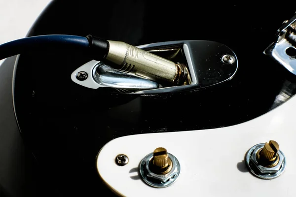 Wire cable jack connected to electronic black and white guitar. — Stock Photo, Image