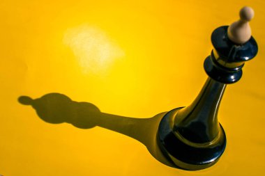 Parlak sarı arka planda gölgesi olan satranç kralı.