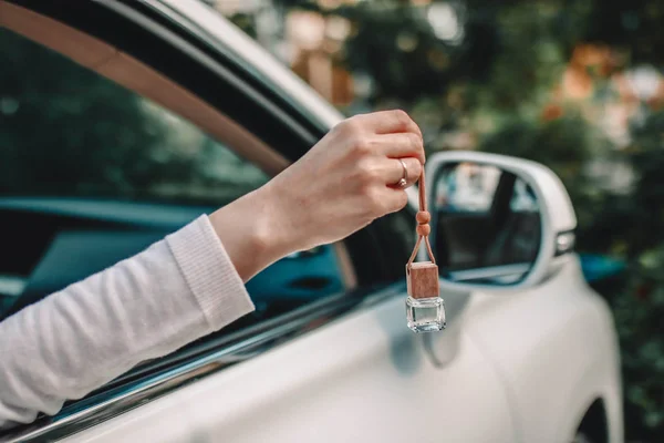 Small glass bottle with car perfume in female hand. Small glass bottle with car perfume hanging near the car. — Stock Photo, Image