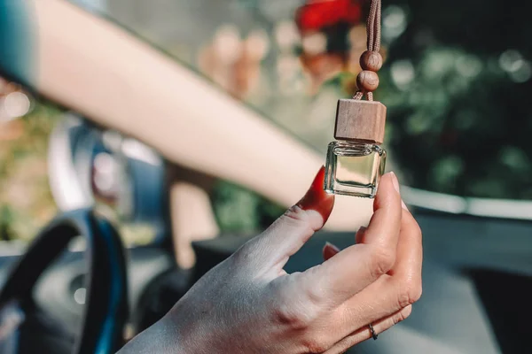 Small glass bottle with car perfume in female hand. Small glass bottle with car perfume hanging in the car.